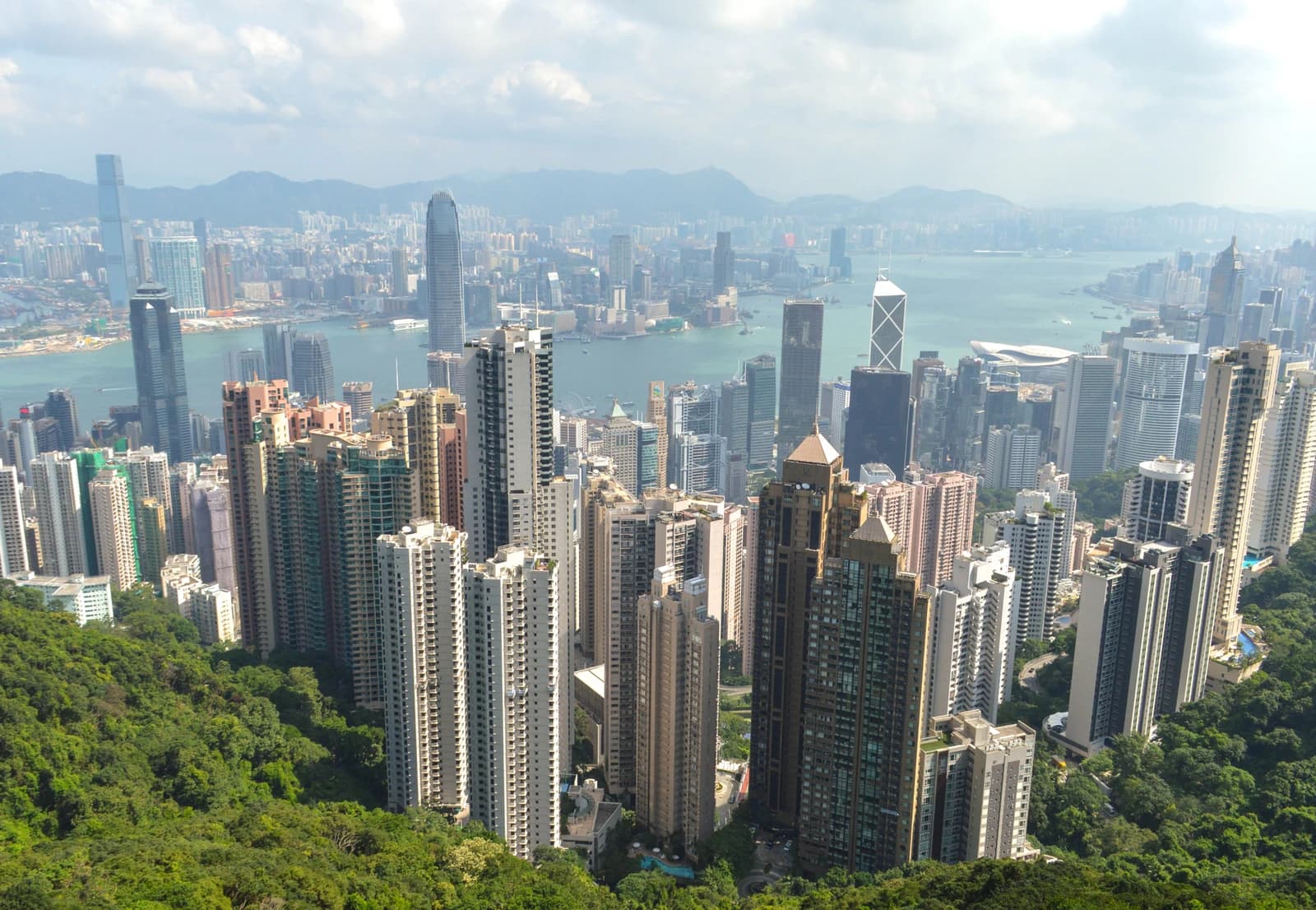 Aerial view of Hong Kong's dense urban landscape with numerous skyscrapers and a body of water.