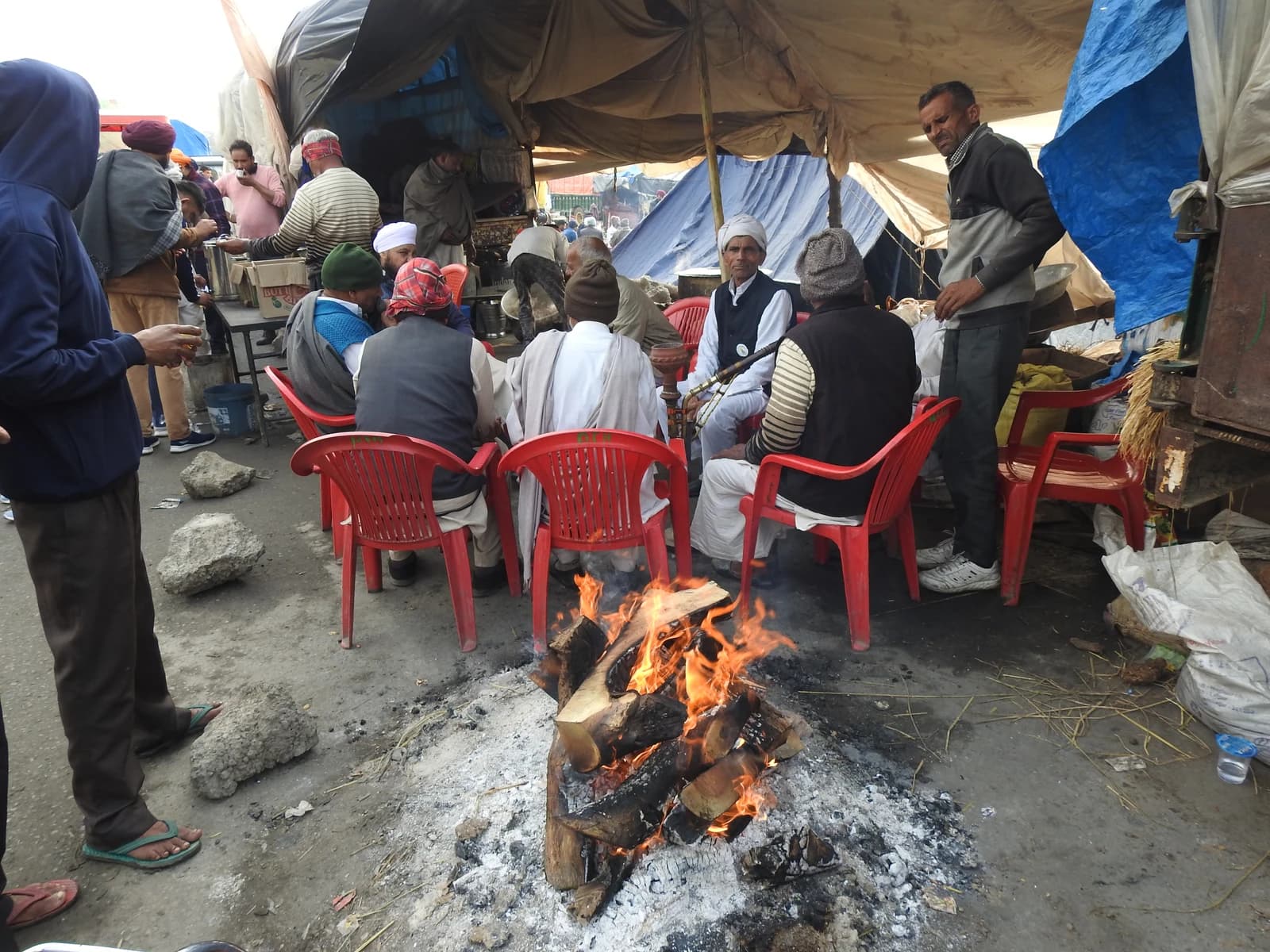 Group of Indian farmers sit around a bonfire under a makeshift tent.