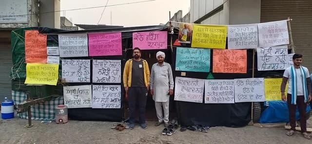 Three farmers standing in front of protest signs at Tikri Border in India.