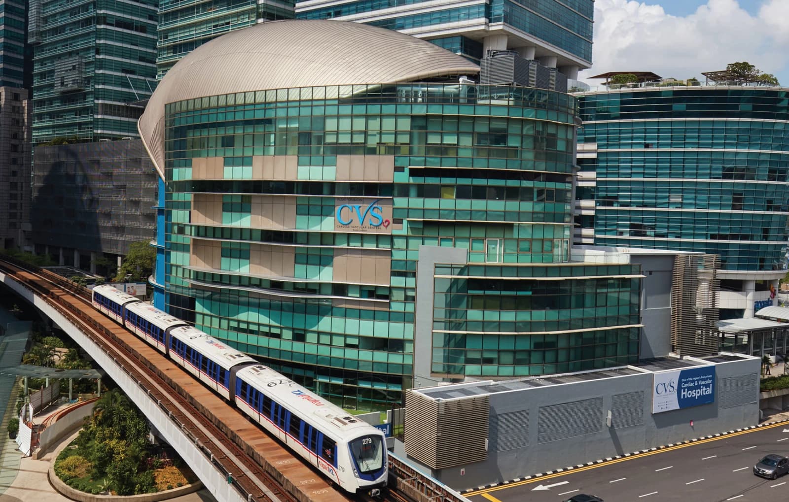 Modern hospital building with glass facade in Malaysia next to an elevated train.