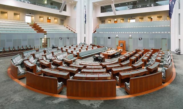 Australian House of Representatives chamber with tiered seating and desks arranged in a horseshoe shape.