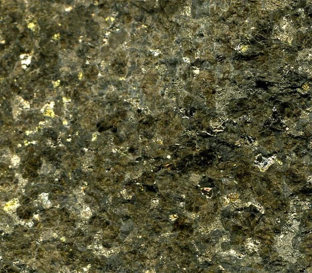 Close-up view of dark gray and gold sulfidic bronzitite platinum-palladium ore.