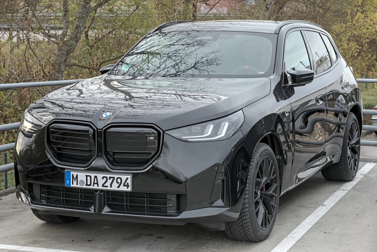 New black BMW X3 M50 SUV parked outdoors with trees in the background.