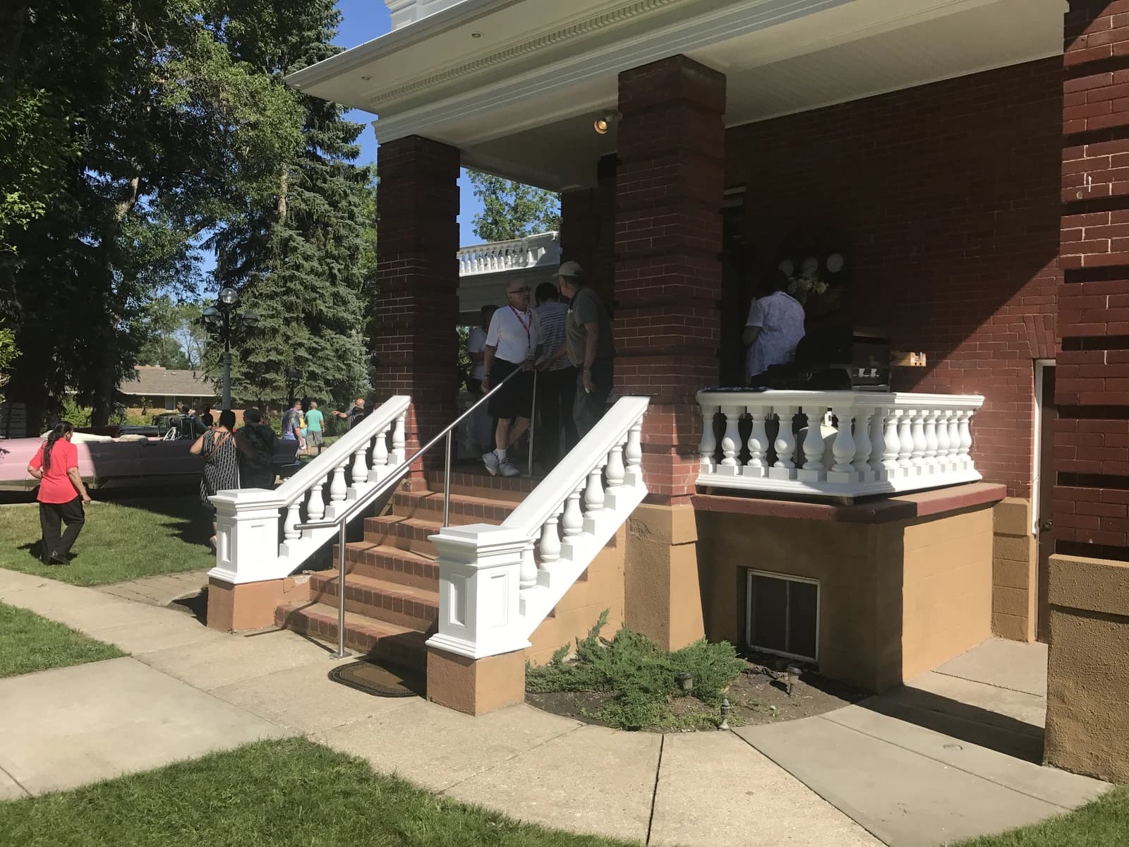 People gathered on the porch and lawn of Magrath Mansion, a brick residence.