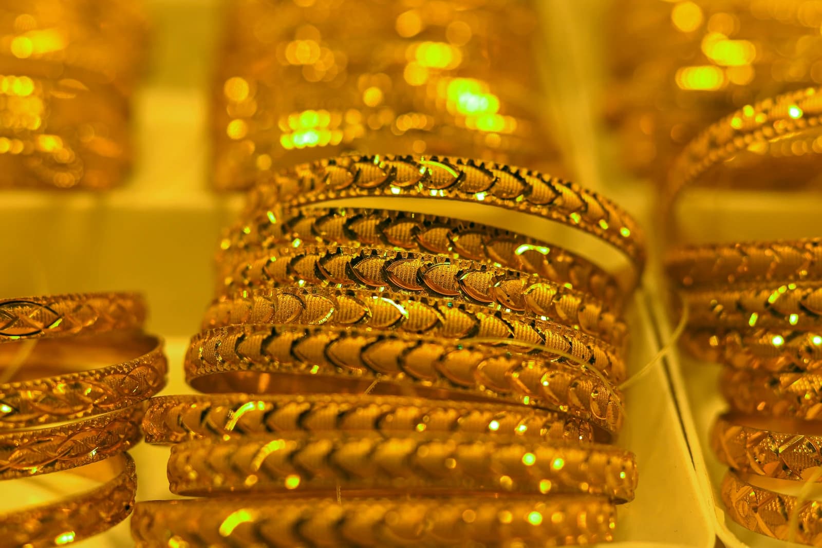 Intricately patterned gold bangles displayed under bright lights in a jewelry store.