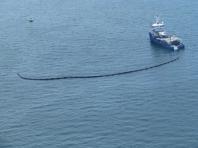 An oil recovery vessel on the ocean deploying a dark containment boom.