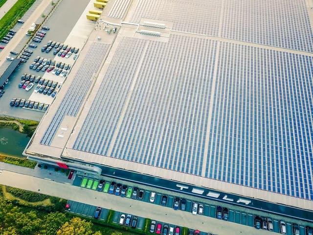 Aerial view of a large Tesla assembly plant with numerous solar panels covering its roof.