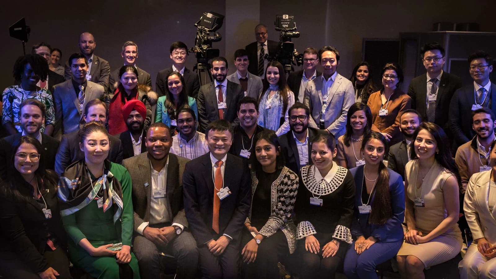 Jack Ma, founder of Alibaba, sits in the front row of a large group of people.