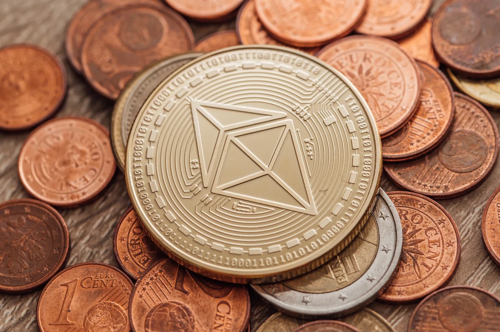 Close-up view of a gold Ethereum coin on a pile of copper and silver euro coins.