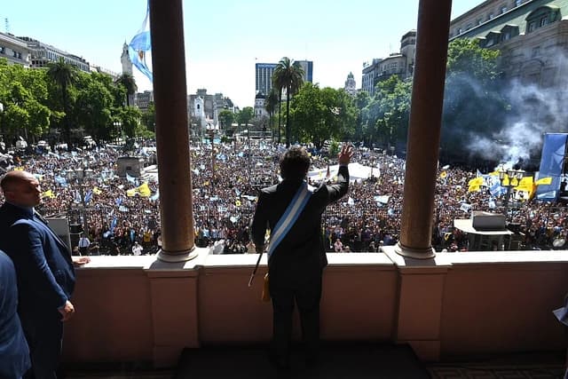 Javier Milei, President of Argentina, waves to a large crowd from a balcony.