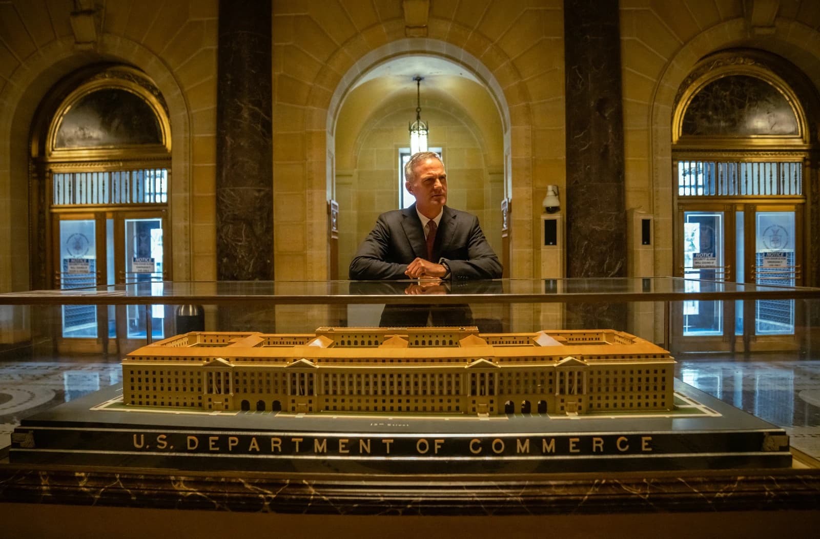 Peter Kyle sitting behind a glass display case with a model building.