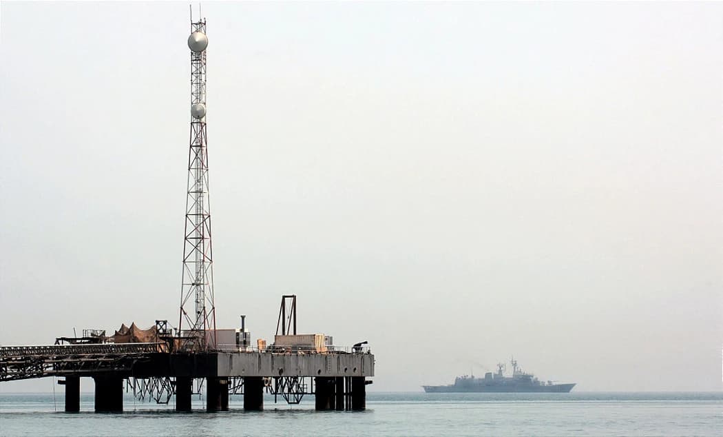A Coalition ship patrols the central Persian Gulf near an oil platform.