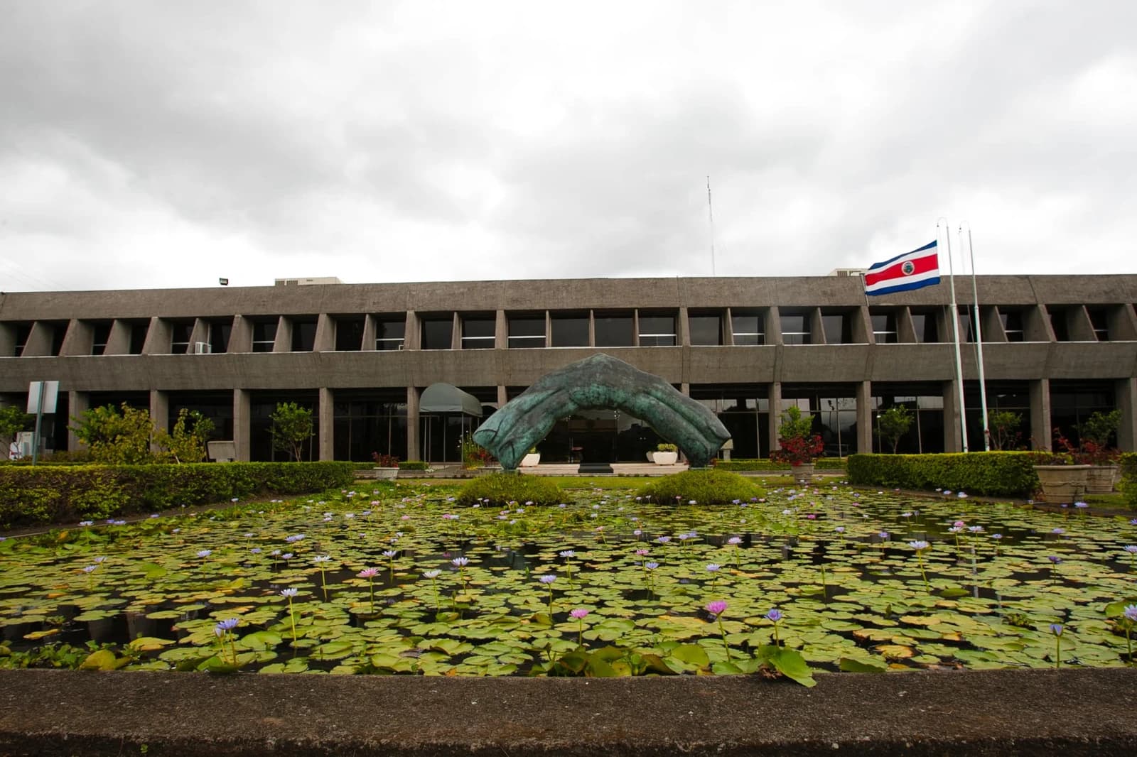 Exterior view of Casa Presidencial in Costa Rica with a pond of water lilies and a flag.