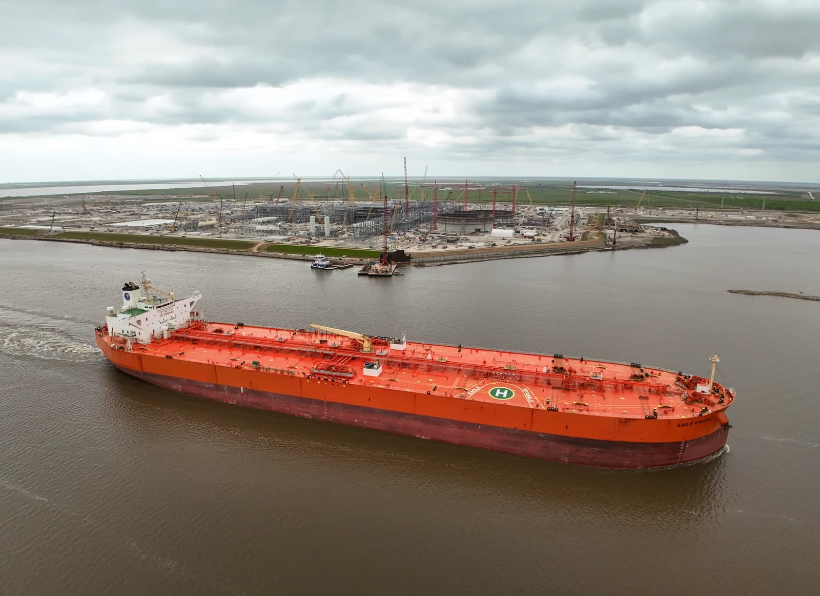 Orange crude oil tanker sailing on water near an industrial facility in Port Arthur, Texas.