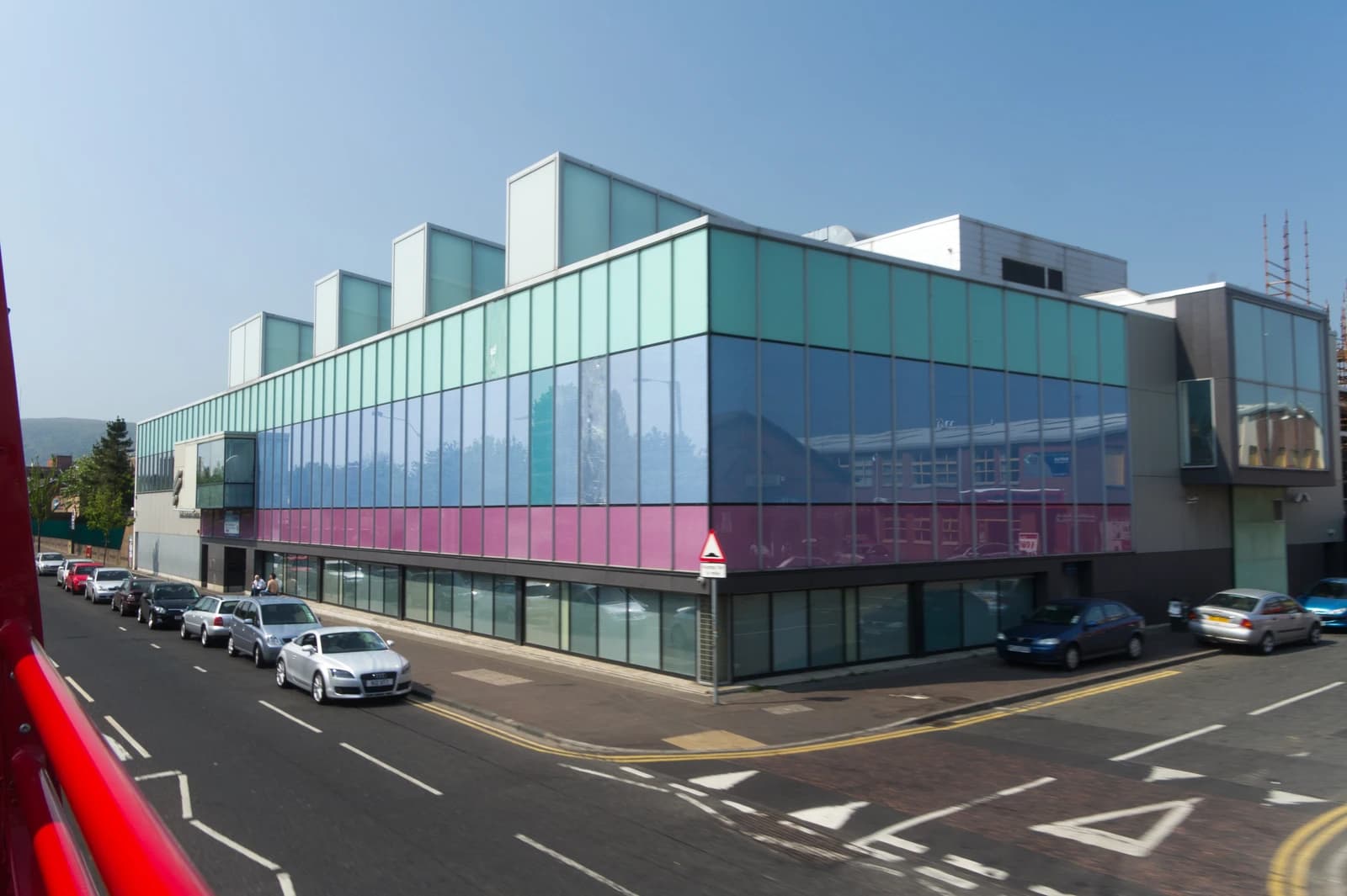 Belfast city street and building with colorful glass facade seen from an open-top bus.