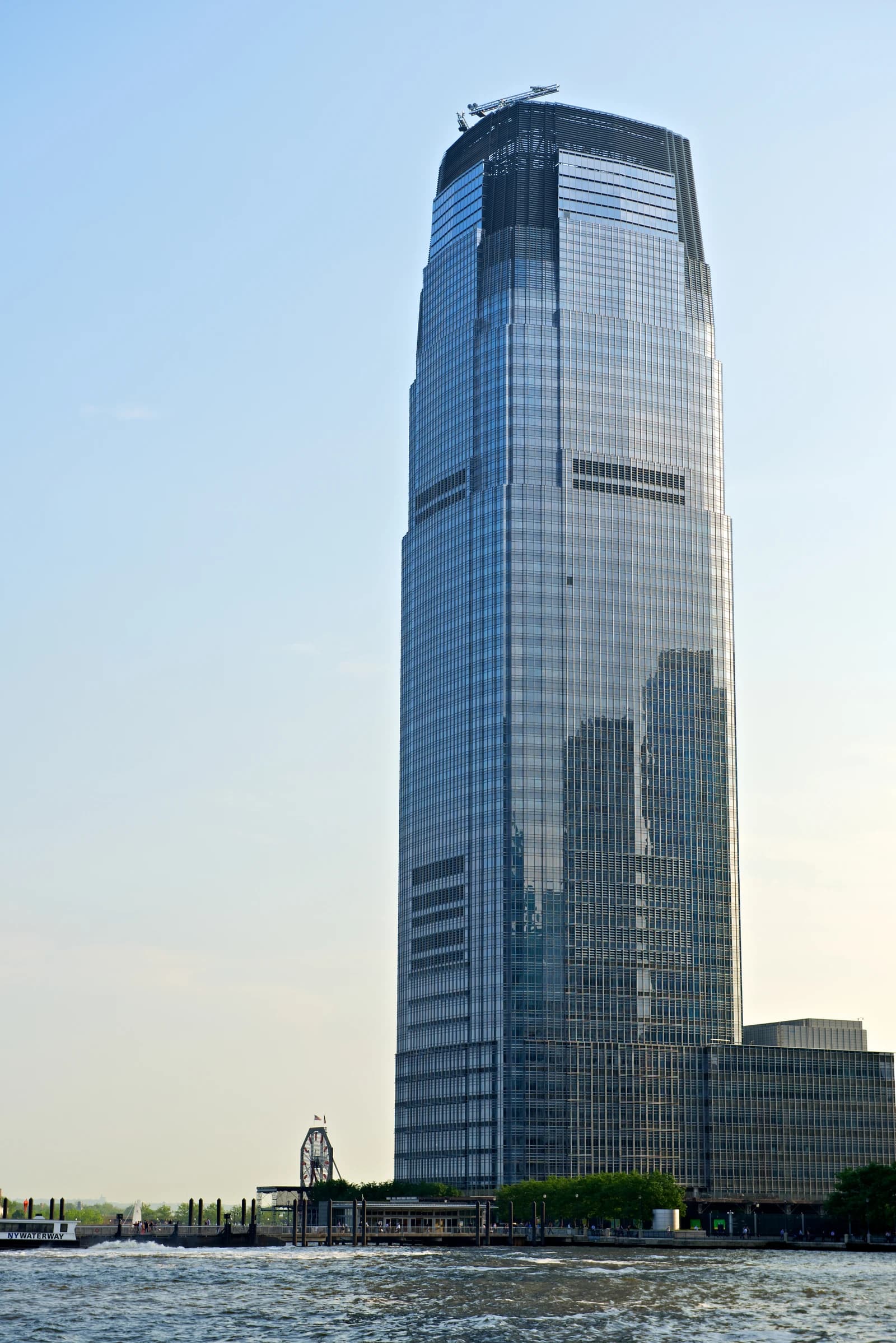 Goldman Sachs Tower, a tall glass skyscraper, viewed from across a body of water.