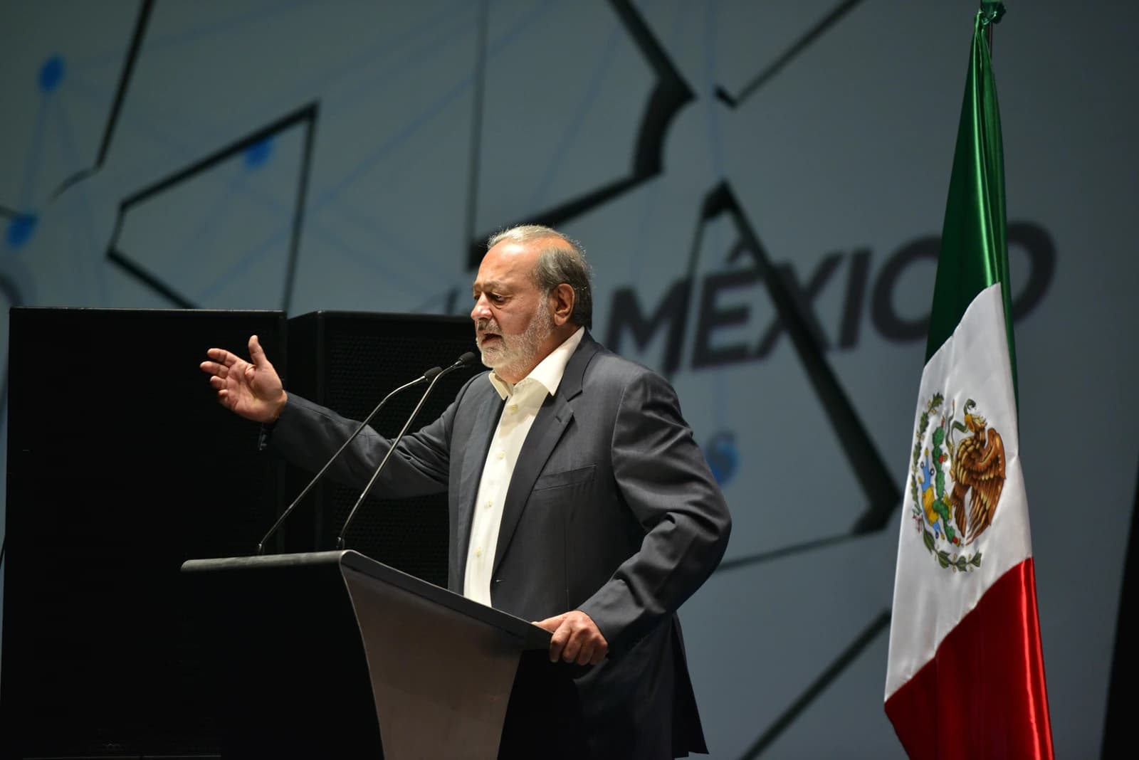 Carlos Slim, Mexican business magnate, speaking at a podium with microphones.