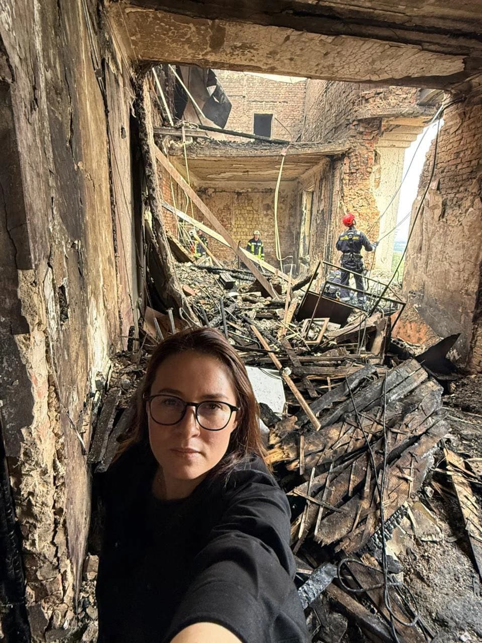 Woman in glasses taking a selfie inside a heavily damaged building in Kyiv.