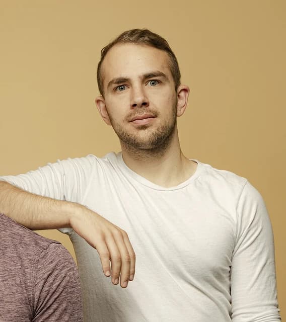 Devin Finzer, CEO of OpenSea, posing with his arm resting on a shoulder.