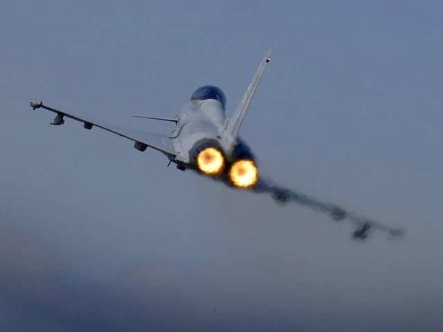 Typhoon F2 fighter jet takes off from RAF Coningsby, afterburners glowing.