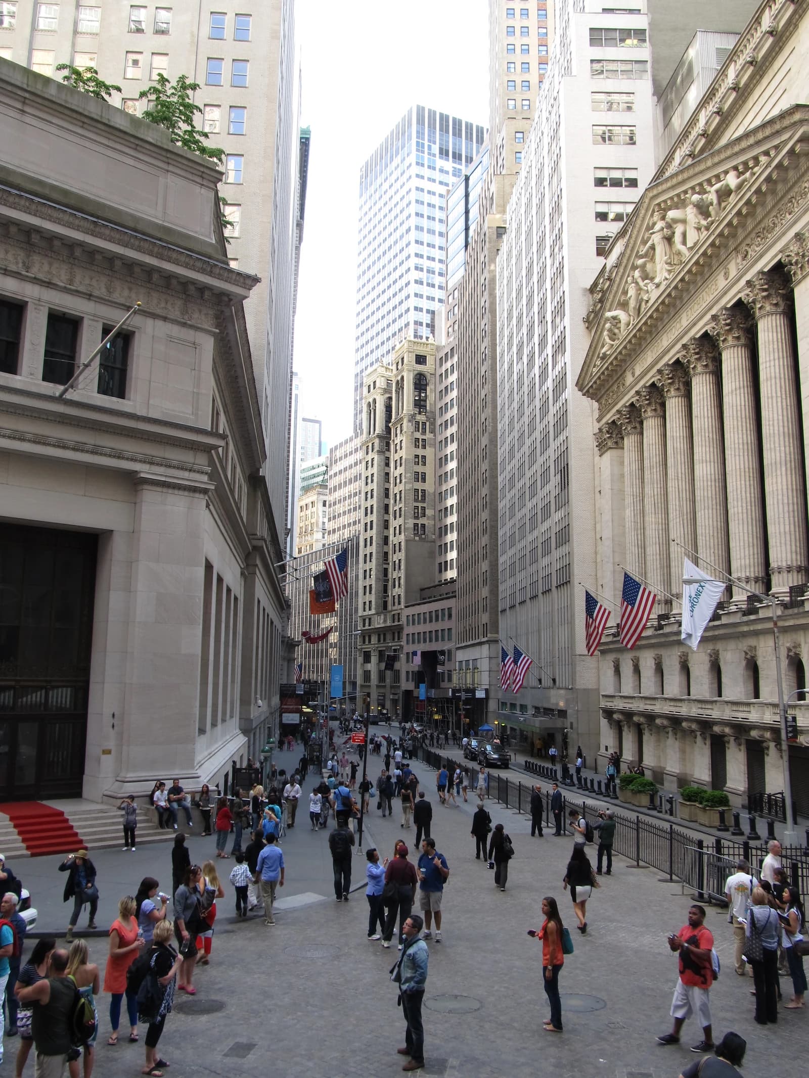 People walking on Broad Street, with the New York Stock Exchange building on the right.