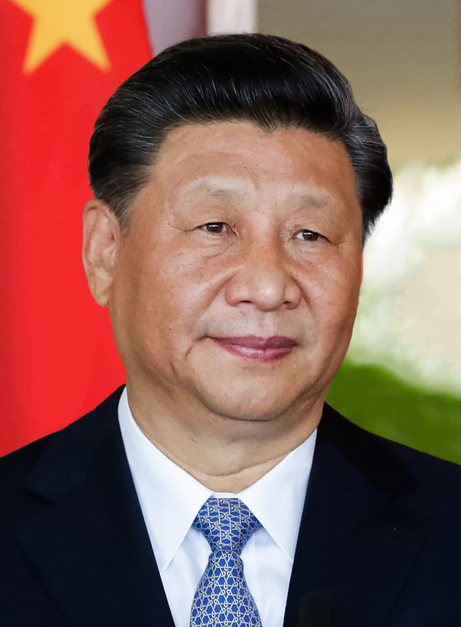 Xi Jinping, President of China, stands smiling with a red flag in the background.