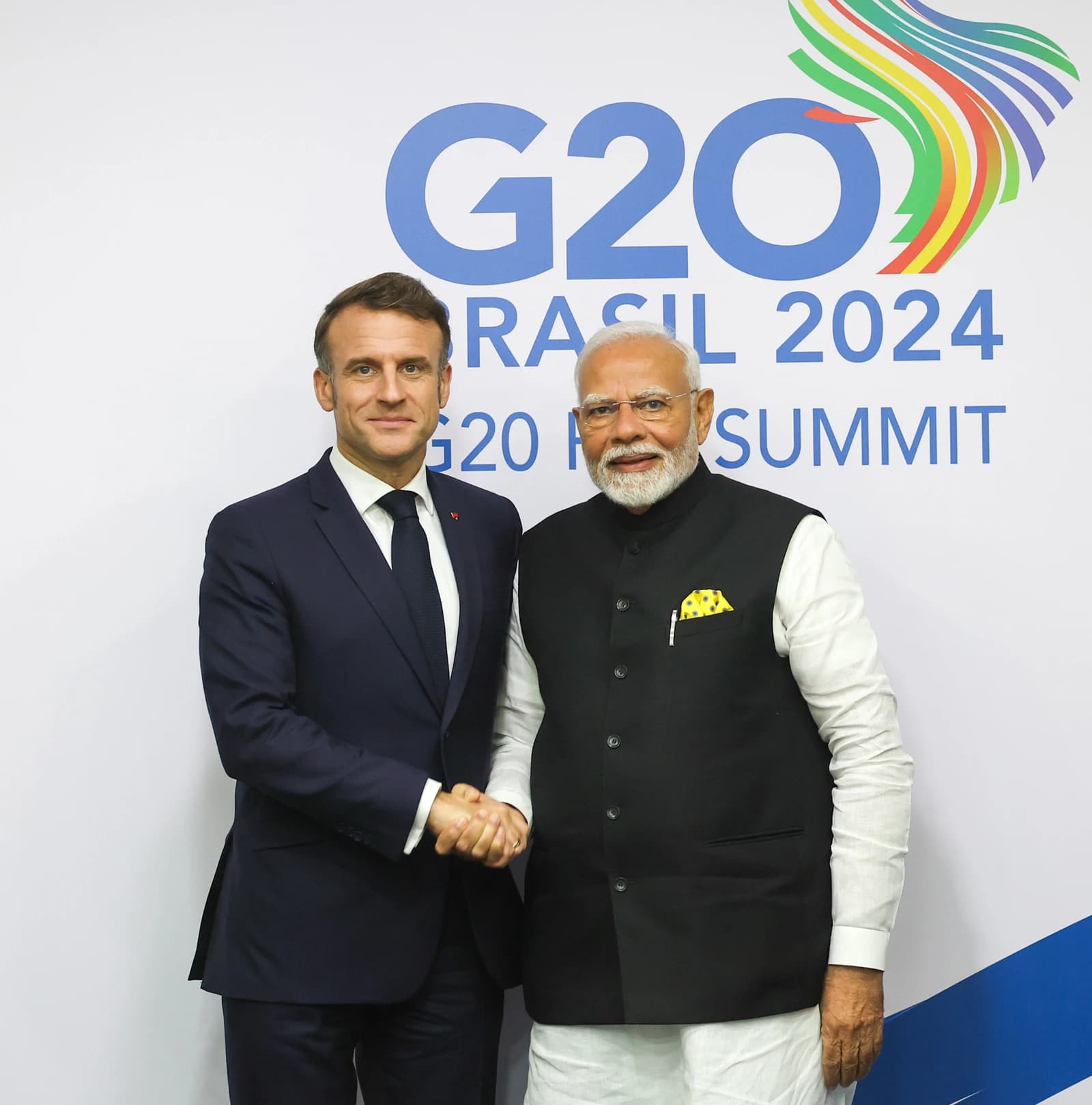 Prime Minister Narendra Modi and President Emmanuel Macron shake hands in front of a G20 logo.