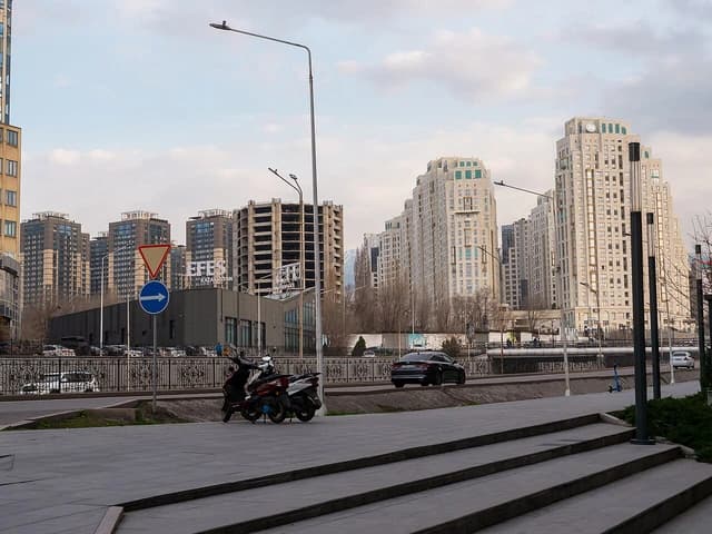Modern apartment buildings and city street with parked motorcycles in Almaty, Kazakhstan.