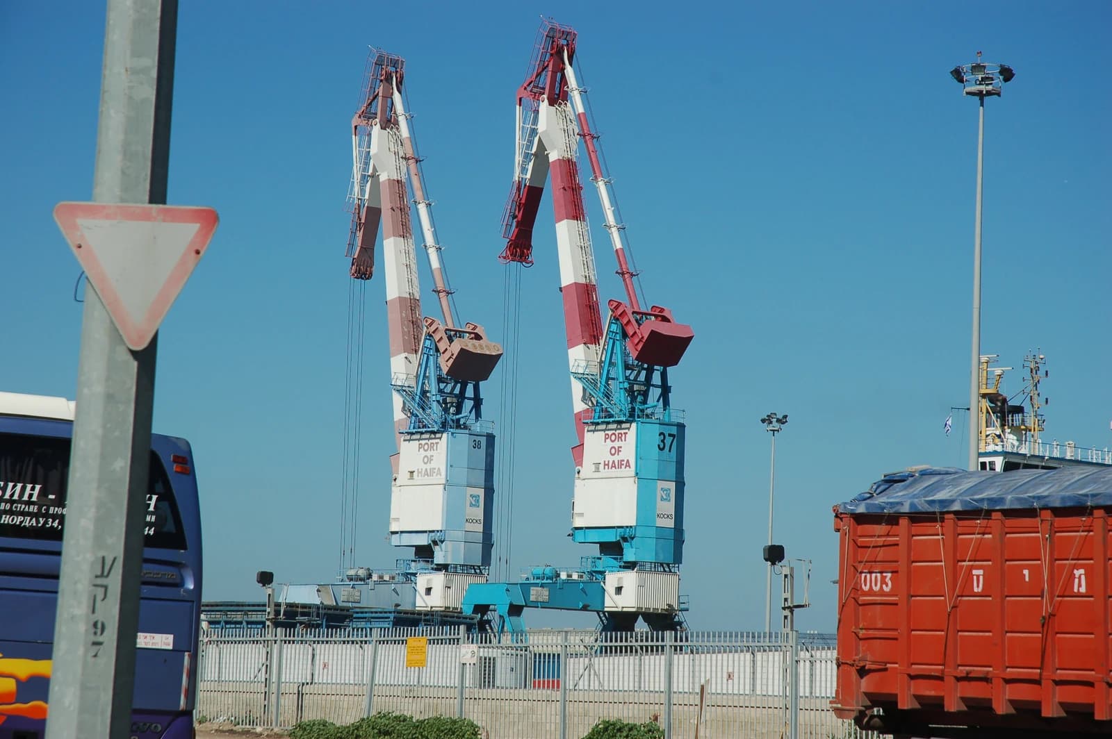 Two red, white, and blue port cranes stand against a bright blue sky at the Port of Haifa.