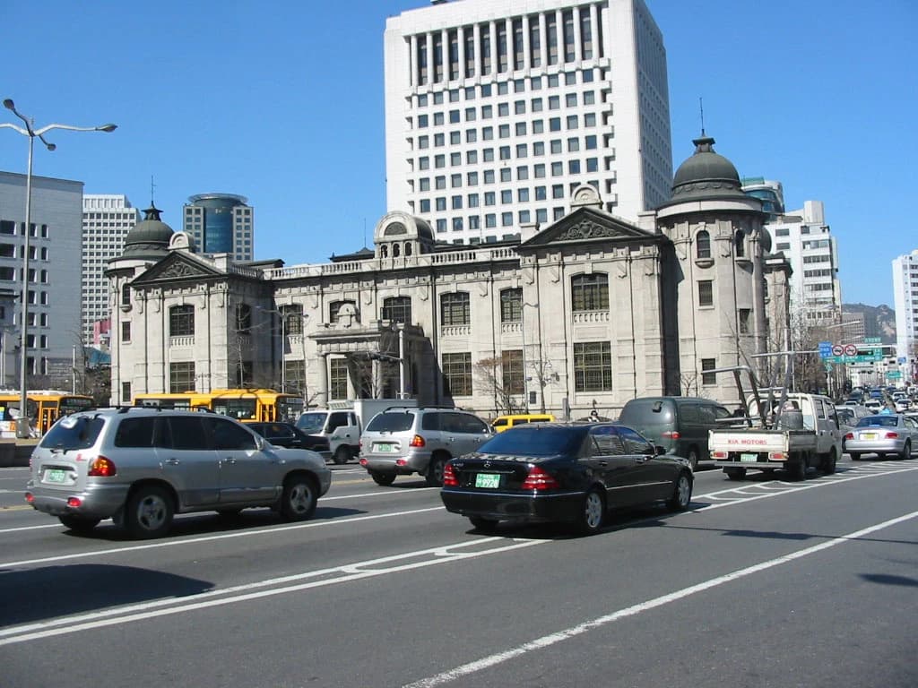 The Bank of Korea building on a sunny day with cars on a busy street.