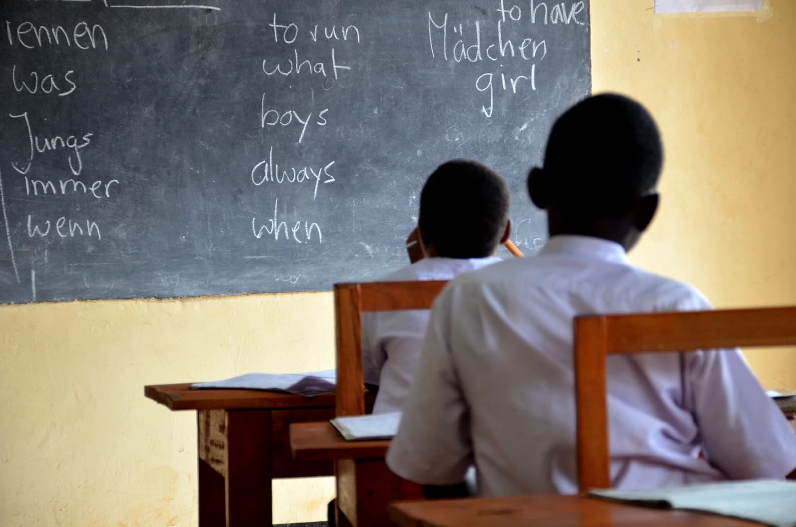 Students in a classroom facing a chalkboard with German and English words written on it.