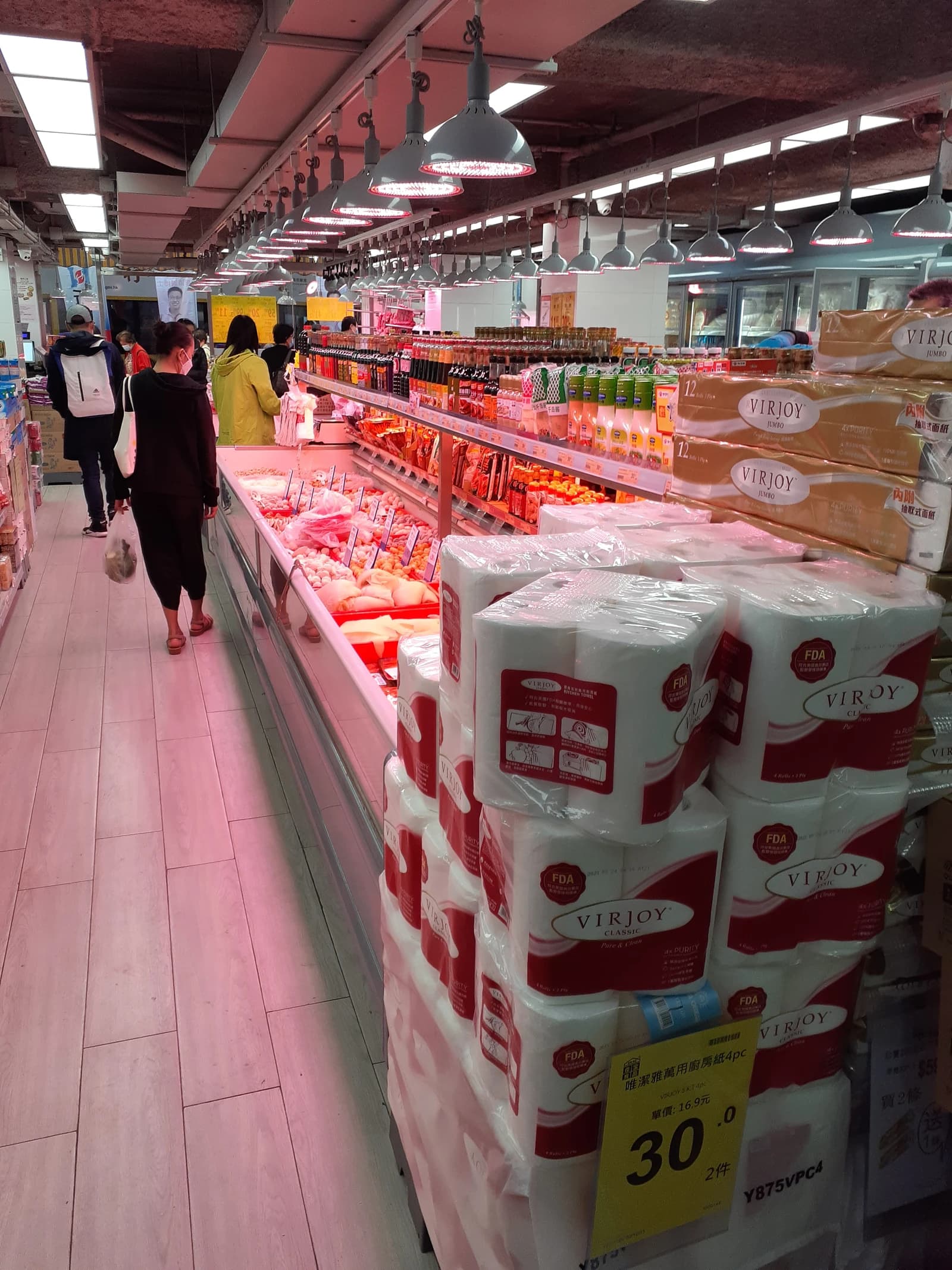 People walking through aisles in a supermarket, shopping for groceries and household goods.