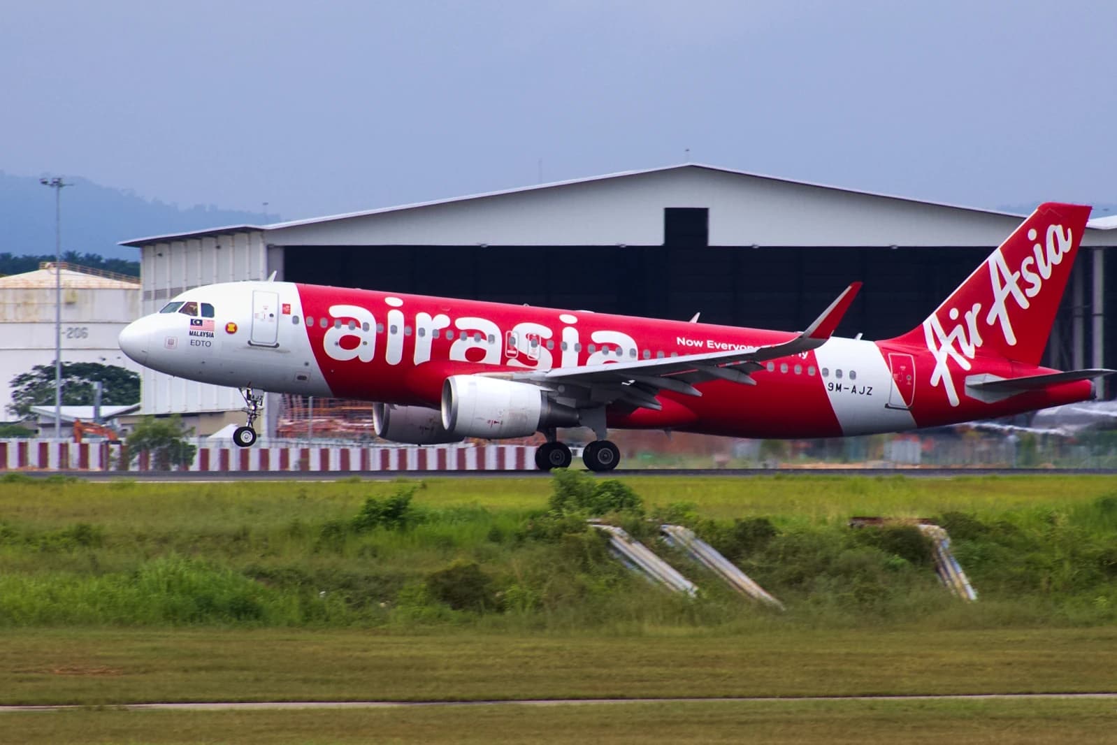 An AirAsia A320 aircraft with registration 9M-AJZ landing on a runway.
