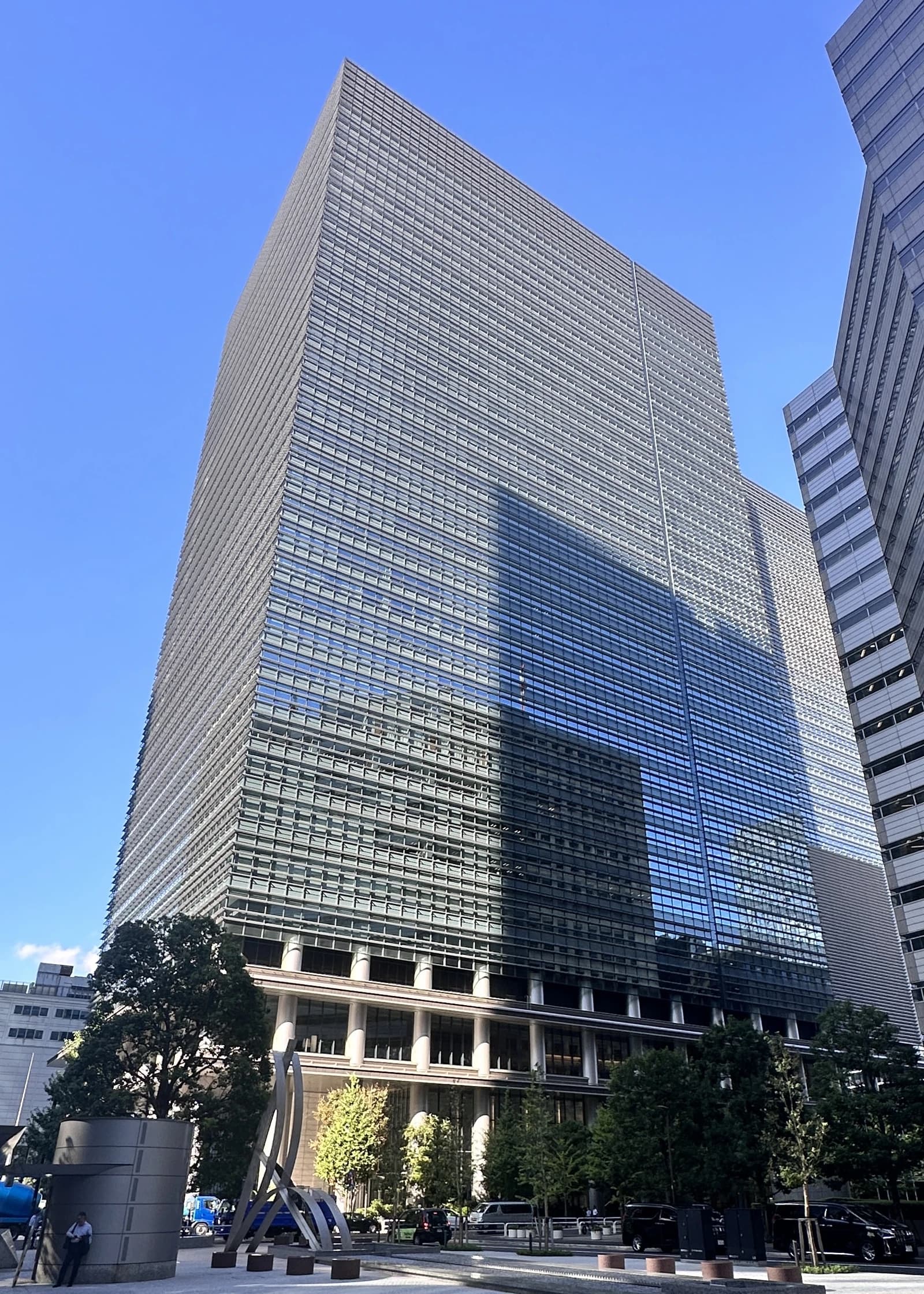 Otemachi Place W building, a large glass and steel structure, stands against a blue sky.