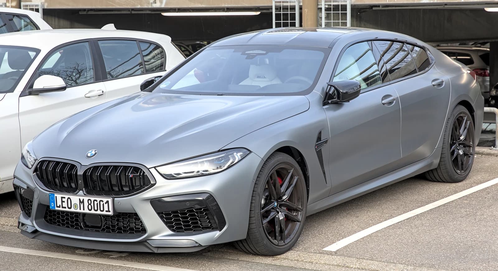 Gray BMW M8 Gran Coupe Competition, front three-quarters view, parked outdoors.