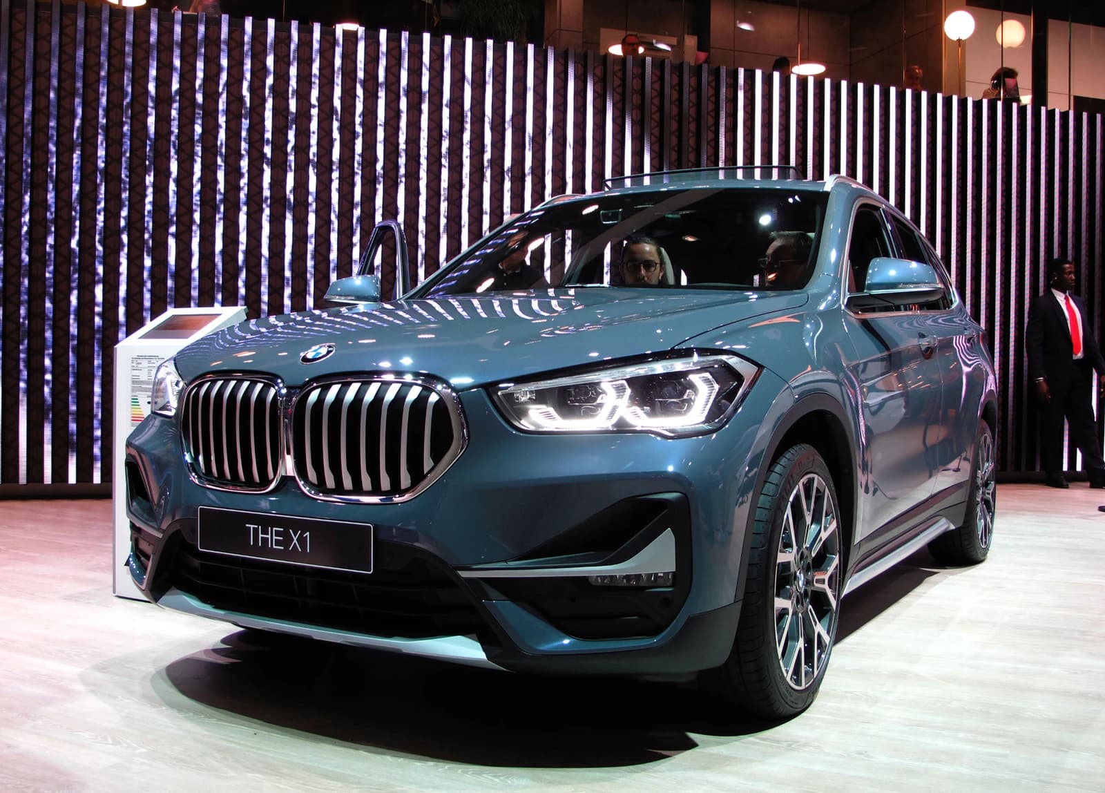 BMW X1 facelift model, a blue compact SUV, on display at an auto show.