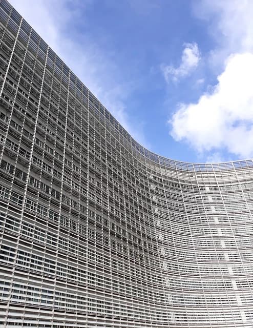 Curving exterior facade of the Berlaymont building under a partly cloudy sky.