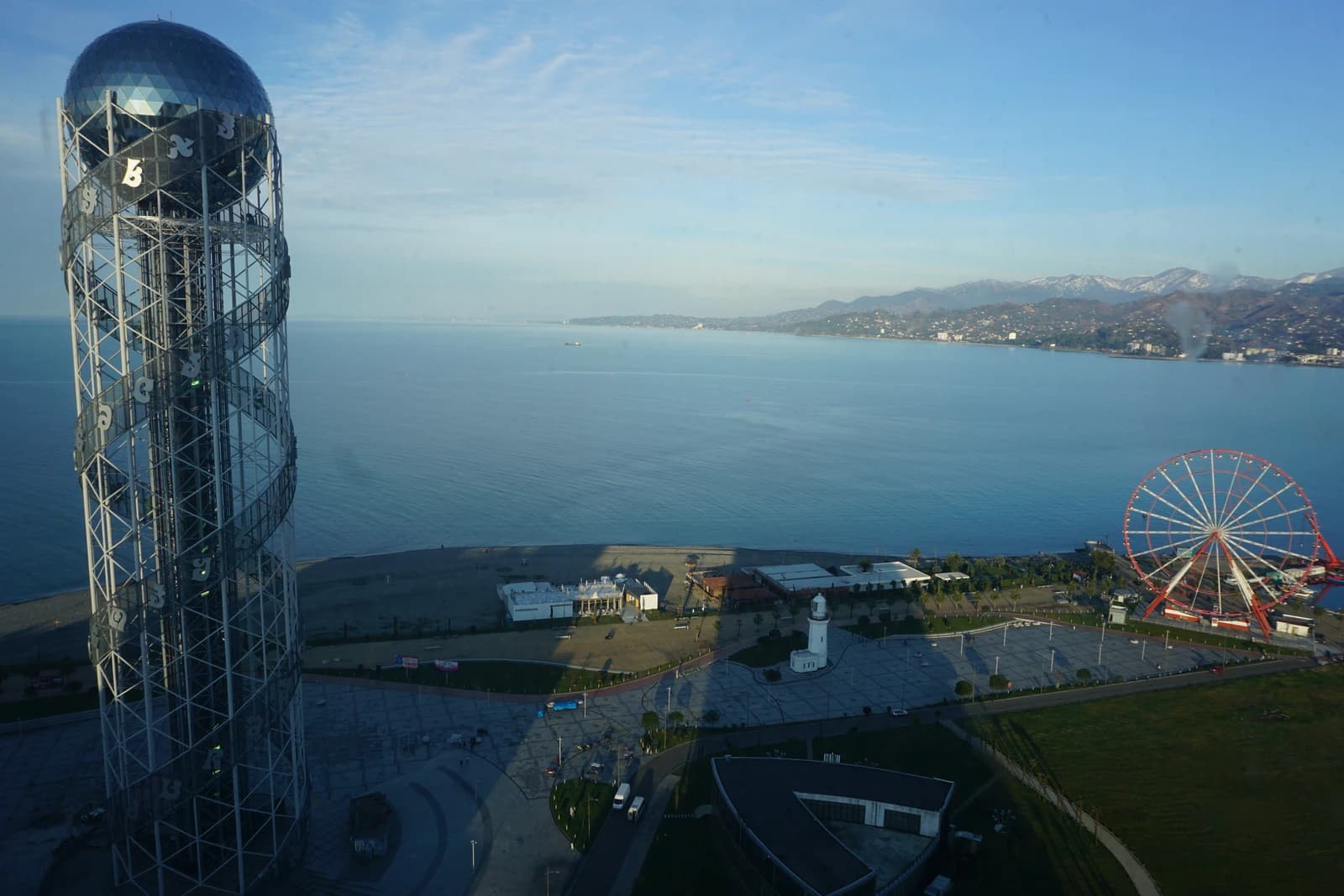 Alphabet Tower and a Ferris wheel stand on the coast of Batumi, Georgia, beside the sea.