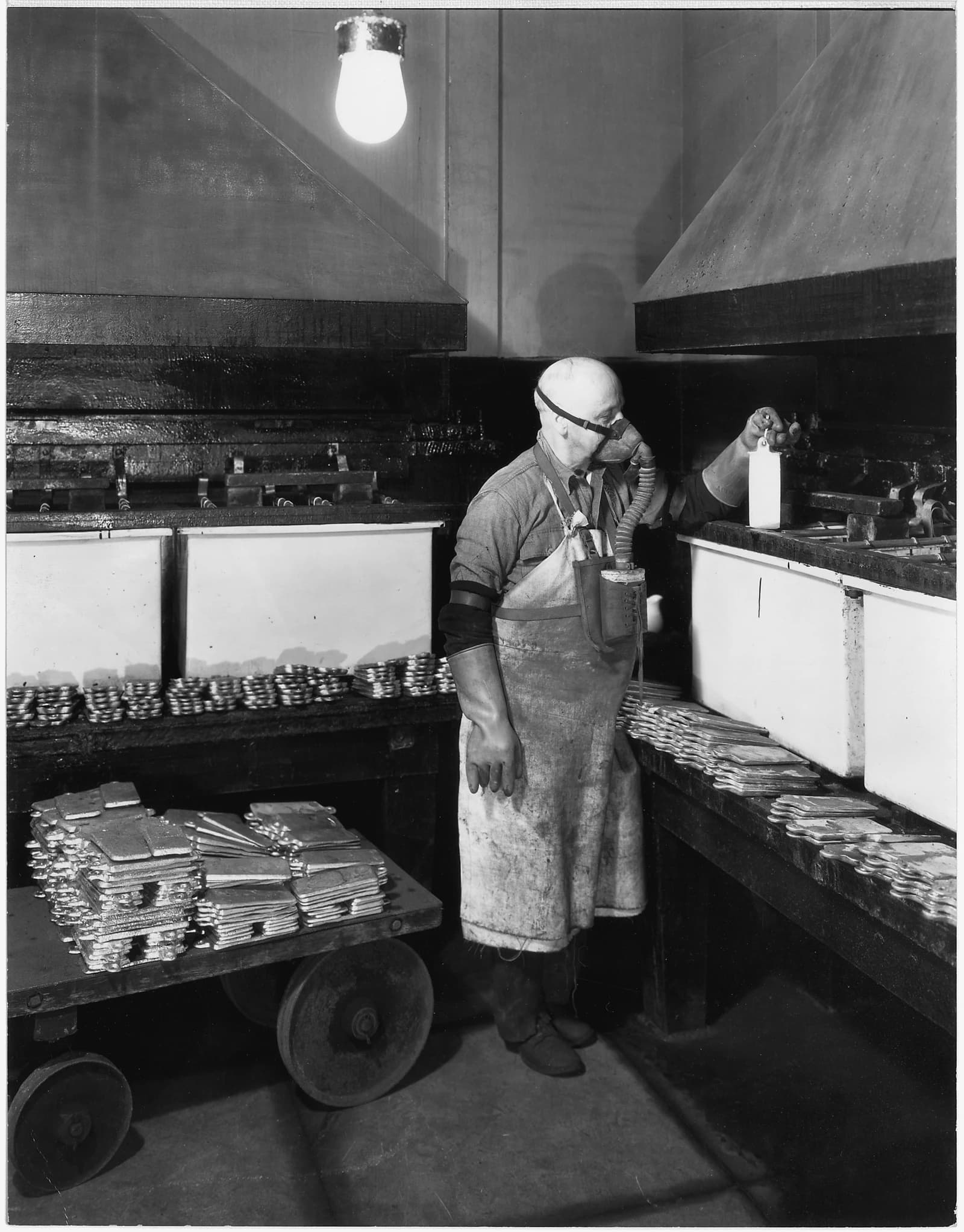 San Francisco Mint worker in a respirator holding a gold bar during electrolytic refining.