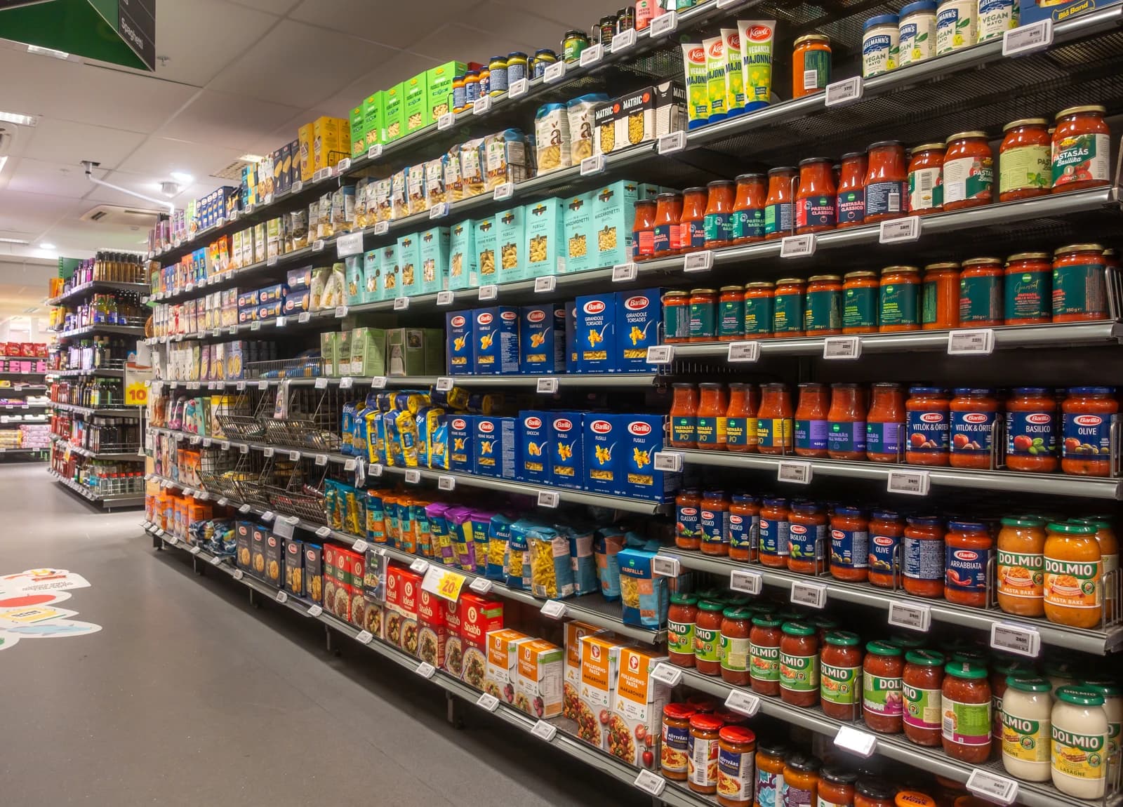 Supermarket aisle displaying rows of pasta, sauces, and other packaged foods.