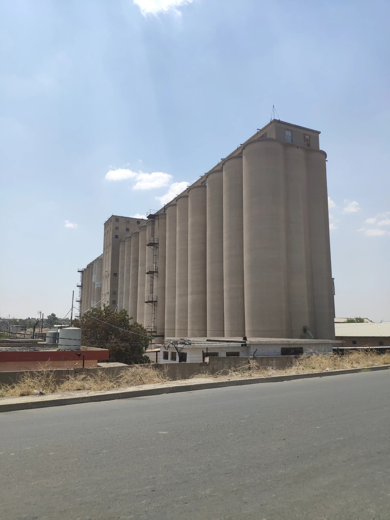 Large industrial grain silos stand tall against a light blue sky.