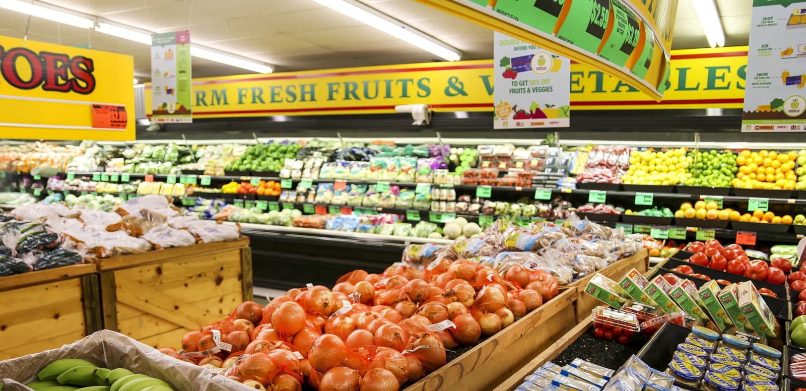 An aisle in a grocery store featuring fresh fruits and vegetables in bins and on shelves.