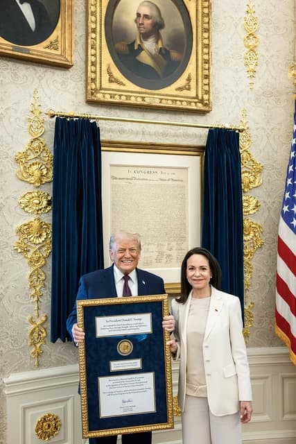 Donald Trump and Maria Corina Machado stand in the Oval Office holding a framed document.