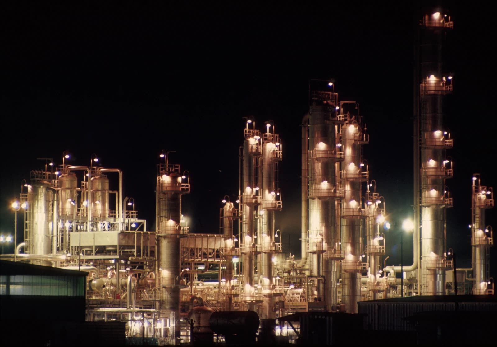 Petroleum refinery with multiple illuminated towers and pipes at night in Texas.