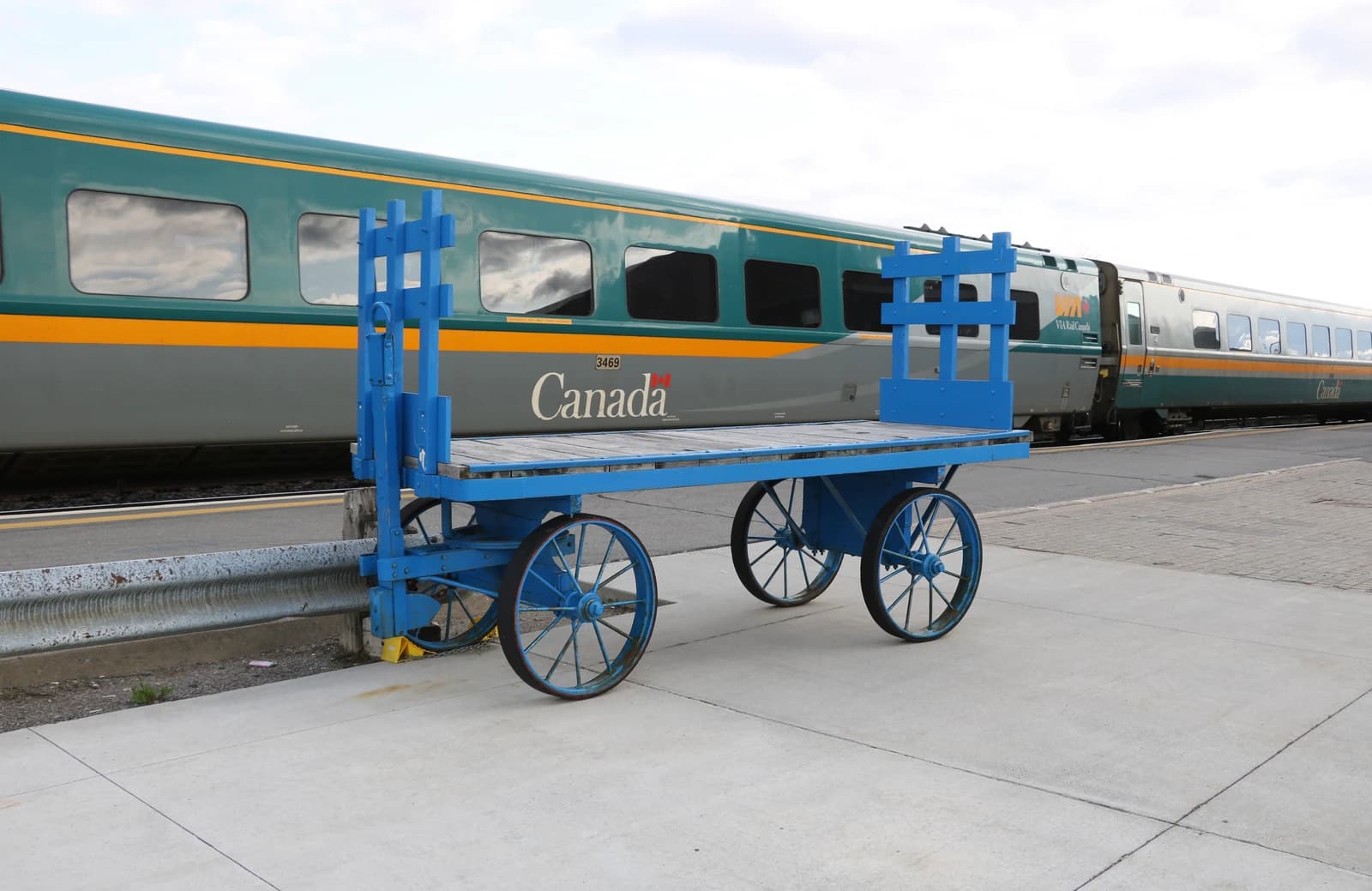Via Rail passenger car on tracks next to an old blue luggage cart.