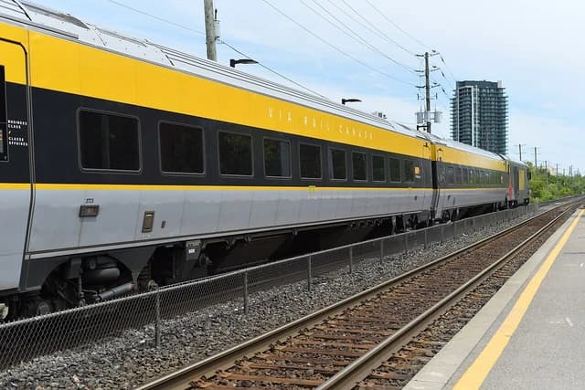 A Via Rail Canada passenger train with yellow and grey cars parked at a station.