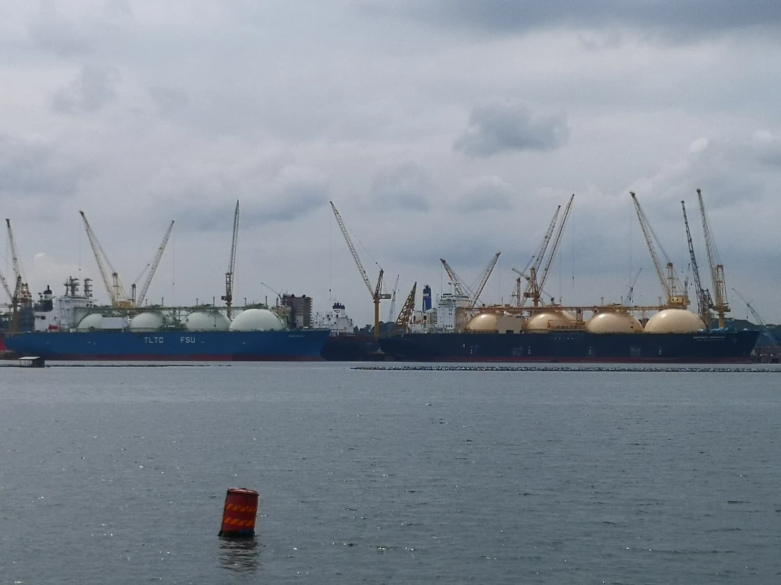 LNG carriers docked, with cranes visible behind them, on a cloudy day.
