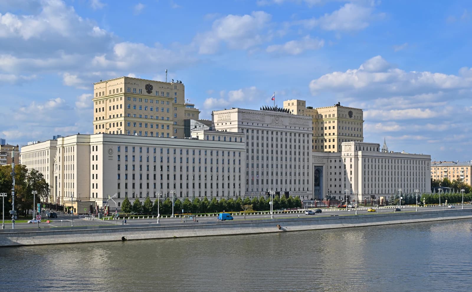 The Russian Ministry of Defence building, a large light-colored complex, stands next to a river.