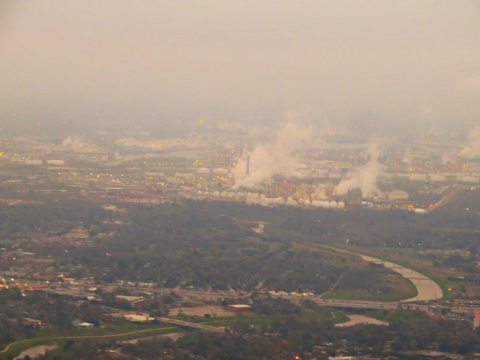 Aerial view of petrochemical refineries emitting steam into a hazy sky in Houston, Texas.