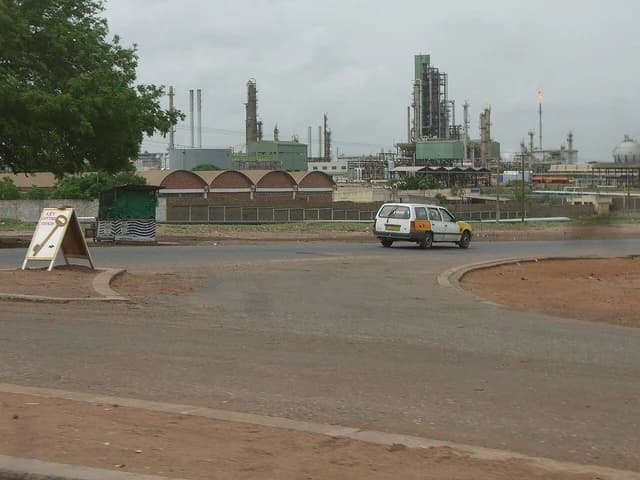 Petroleum refinery with multiple towers and pipes under a cloudy sky.